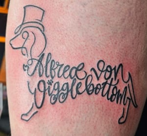 Tattoo of a dachshund in a top hat drawn from the name Alfred von Wigglebottom
